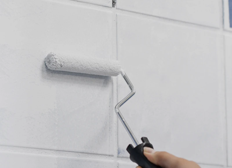 Small roller applying white paint to square tiles.
