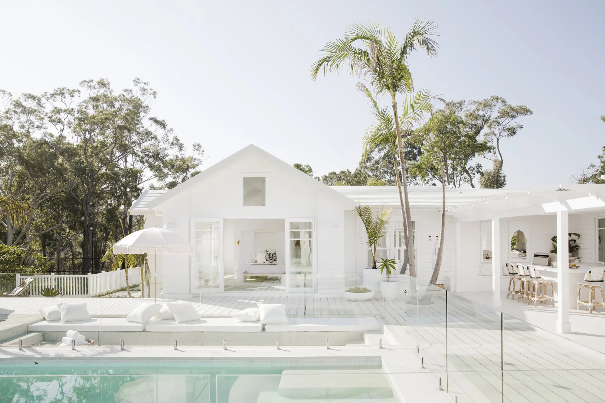 A white Hamptons style home with a pool in front of it