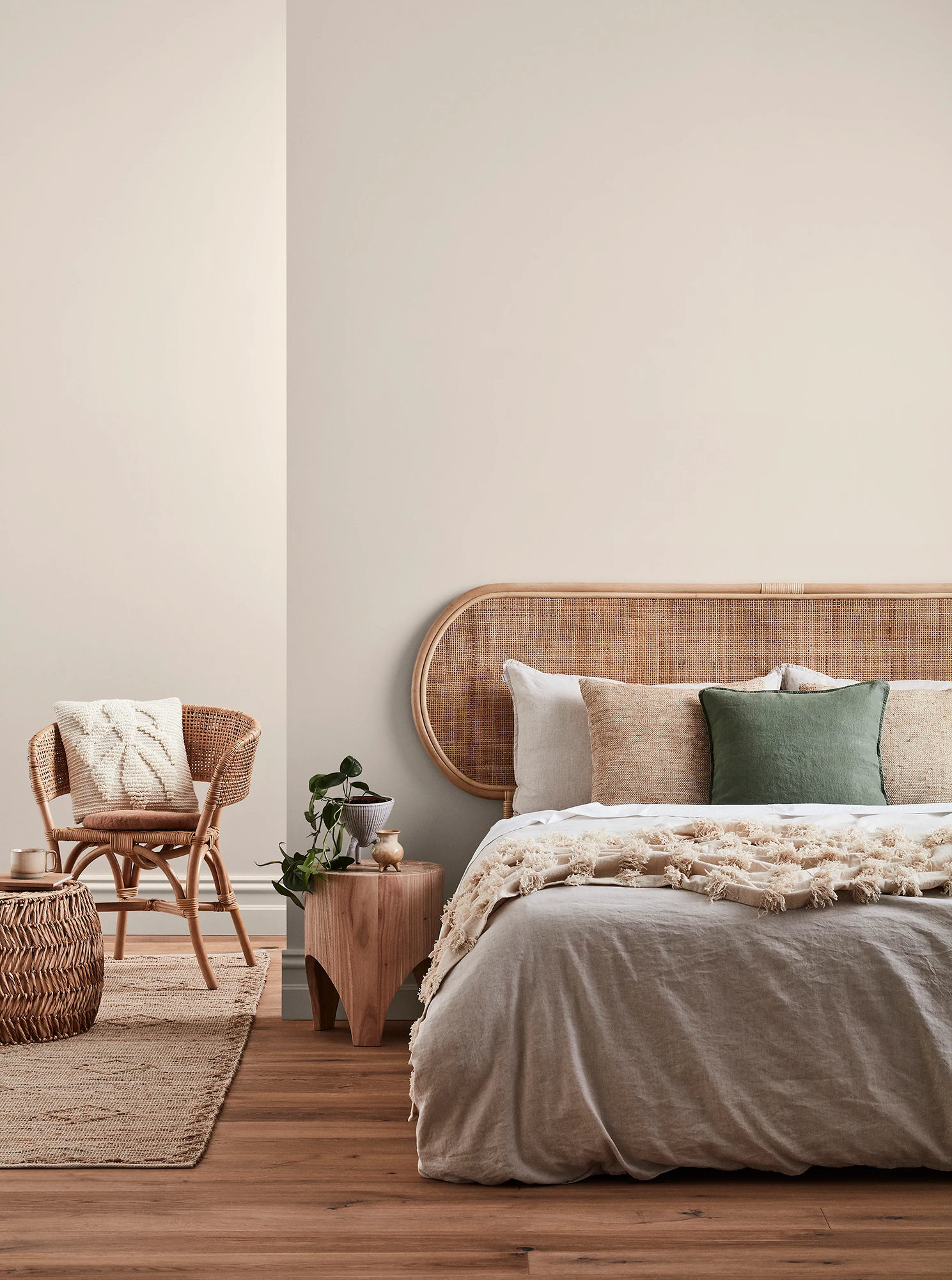 Neutral-coloured bedroom with rattan headboard and chair and neutral linens.