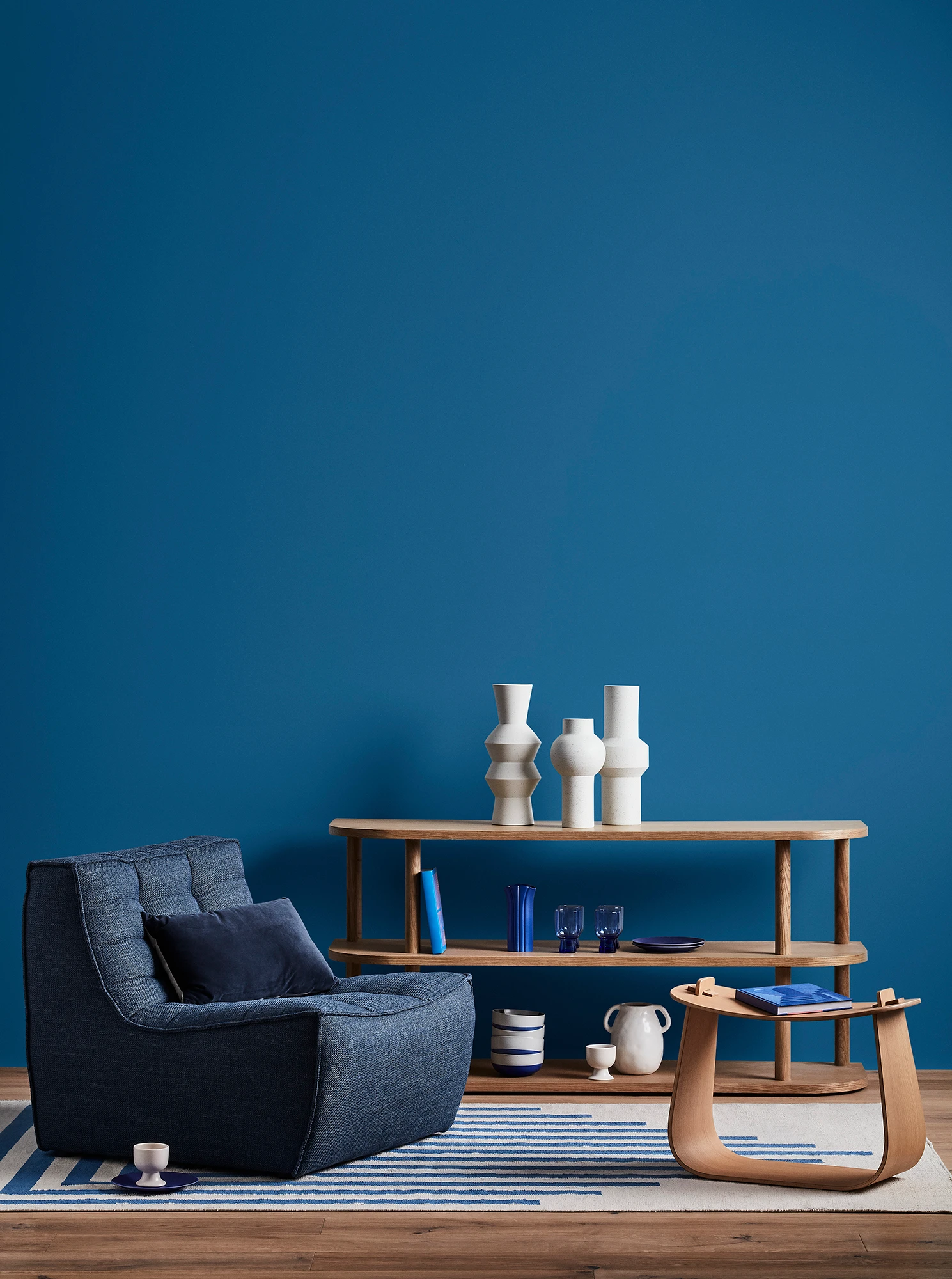 Blue living room with blue armchair, wooden coffee table and shelves with blue and white decor. 