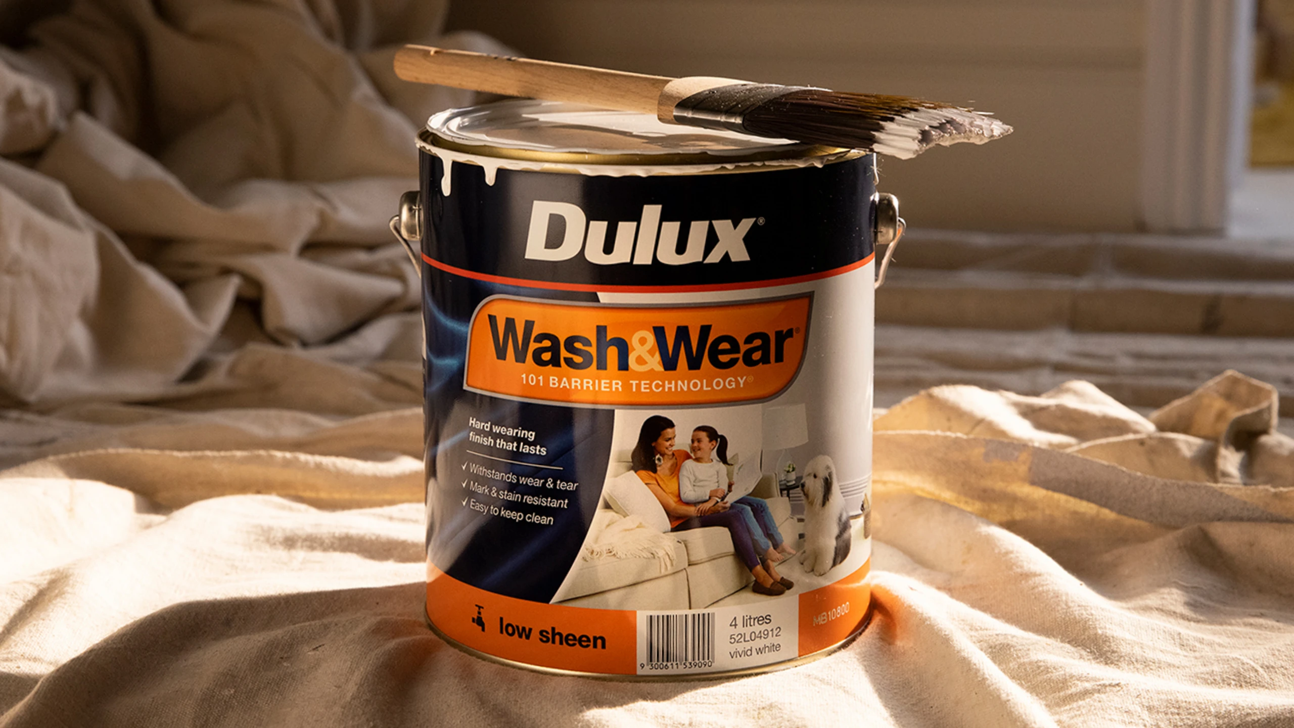A tin of beige Dulux Wash&Wear paint with a brush and a drop sheet.