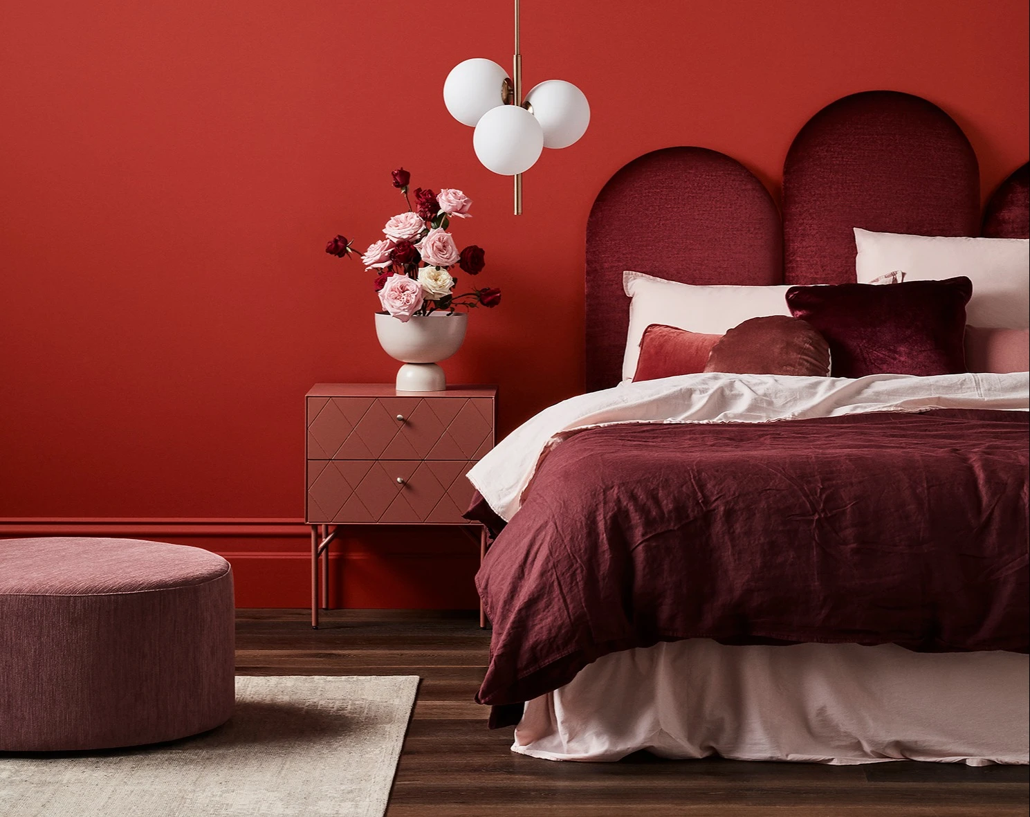 Red themed bedroom with velvet bed, bedside table and flowers in a vase.