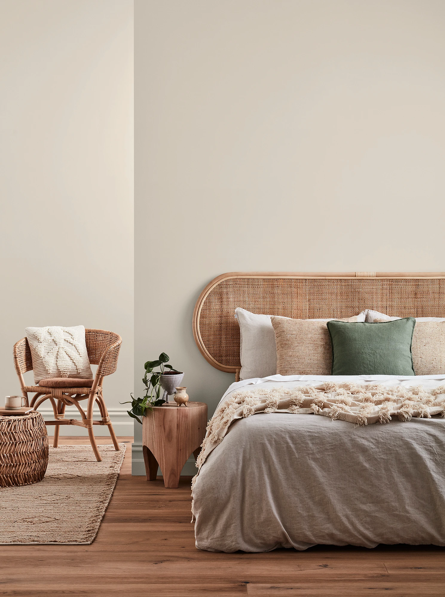 Neutral-coloured bedroom with rattan headboard and chair and neutral linens.