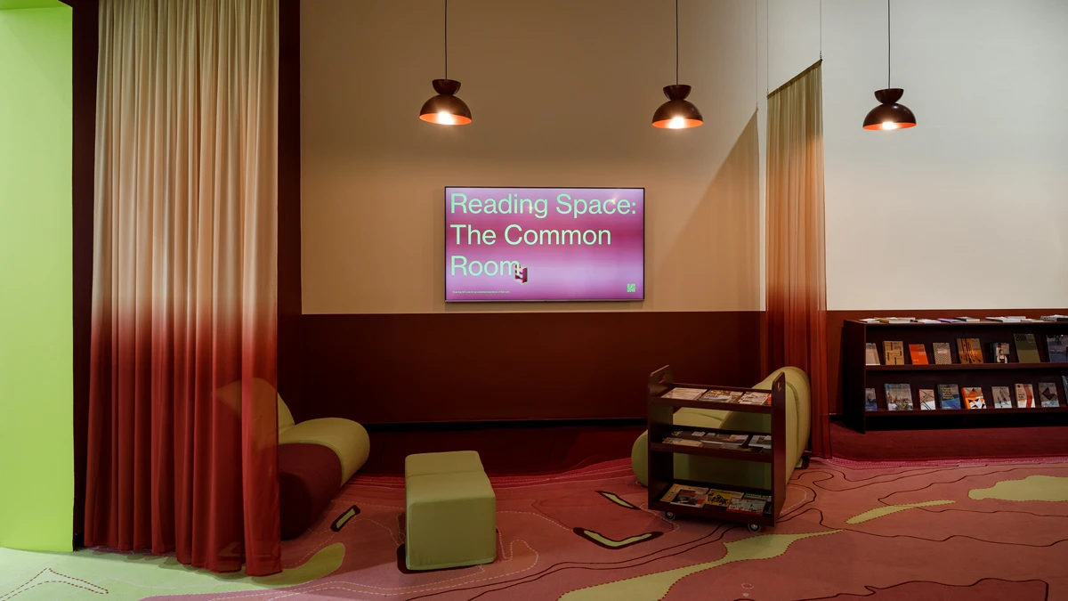 Low-lit reading space with chairs and curtains. Book shelf to right of reading area. 