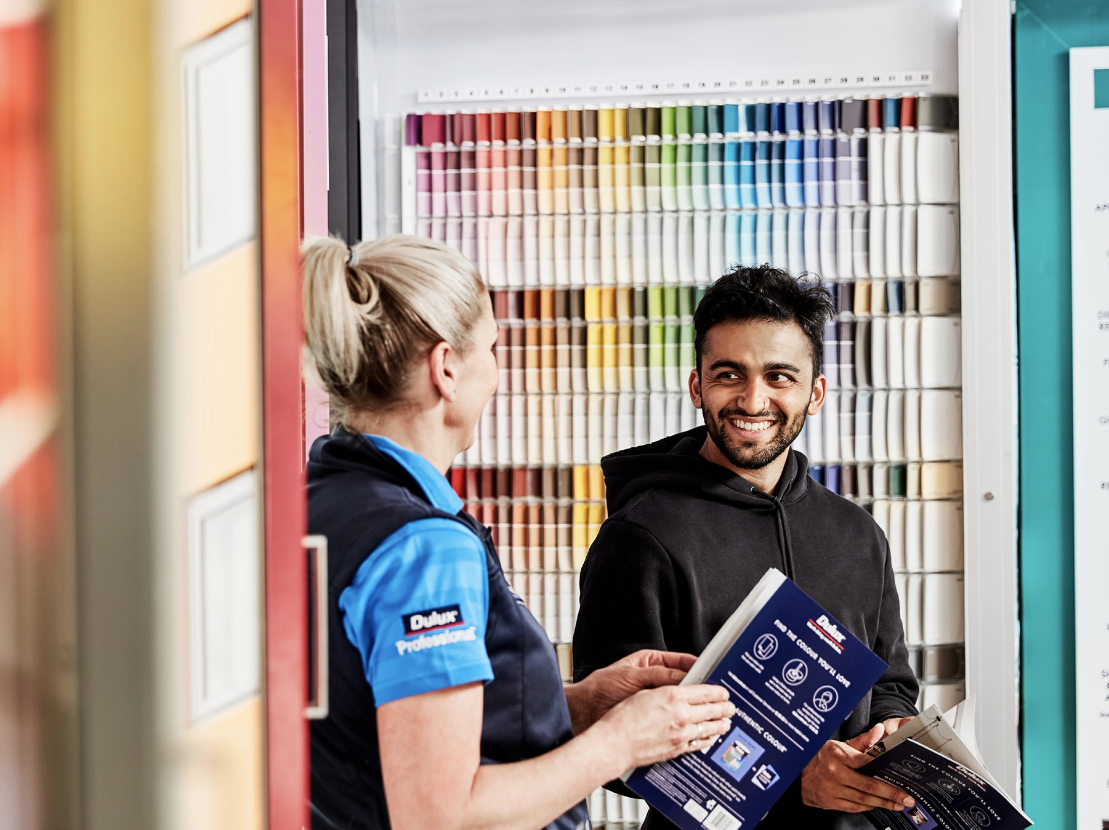 Dulux store staff talking to a painter in front of the colour chip wall