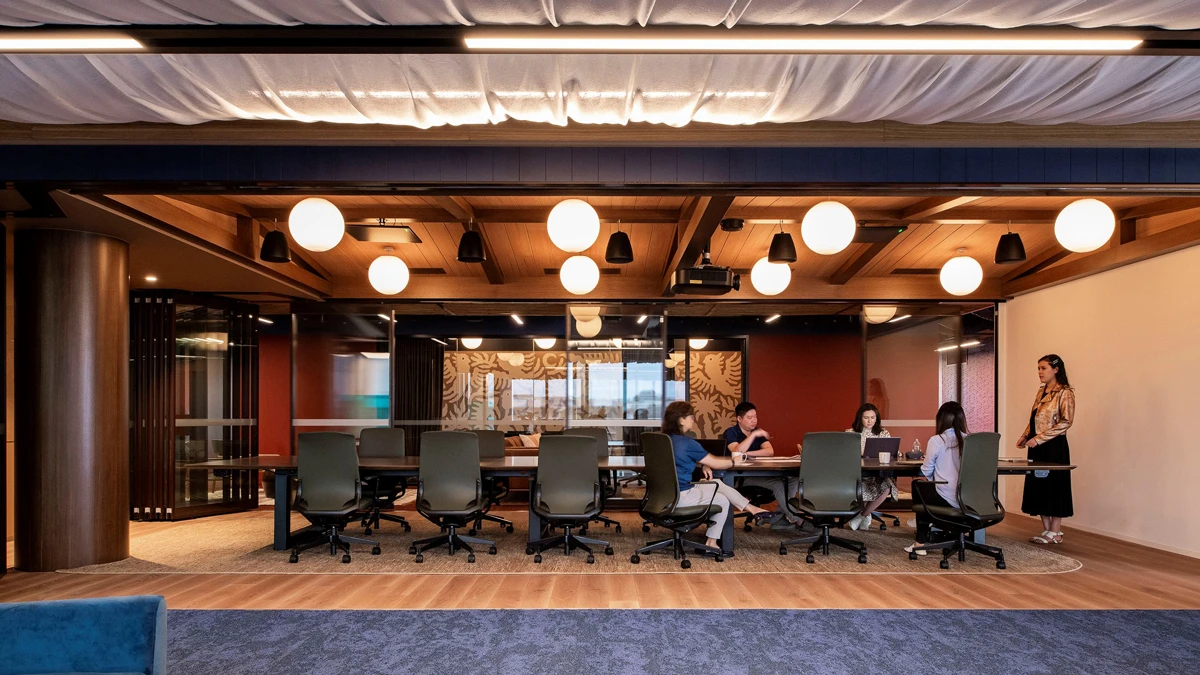 Large boardroom with sphere lights hanging from roof and people sitting at meeting chairs. 