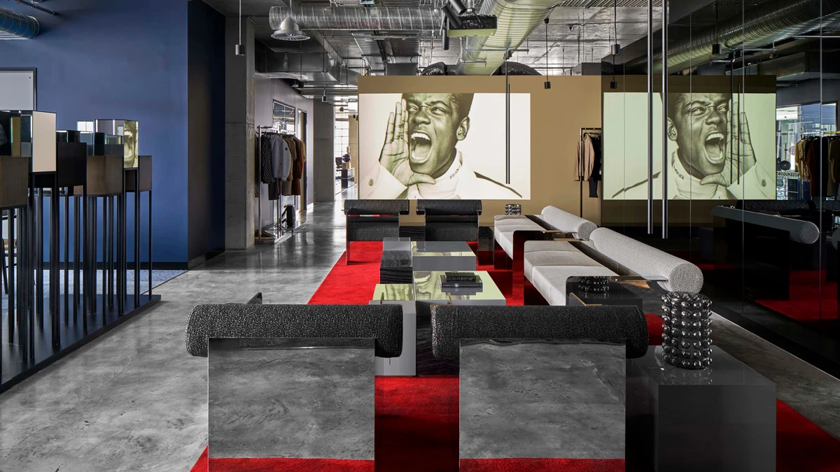 Designer lounges in open space, projected image of man shouting on wall in background. 