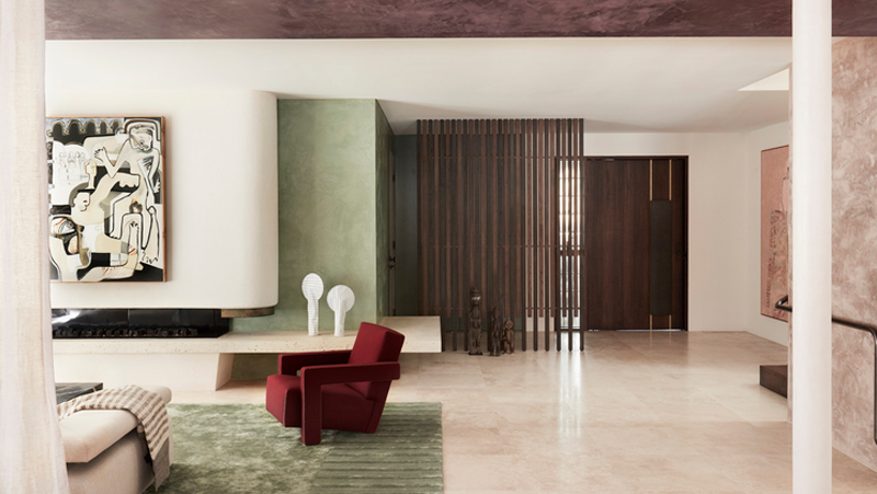 Modern living area with cream and green walls, terrazzo floors, green rug, red armchair.