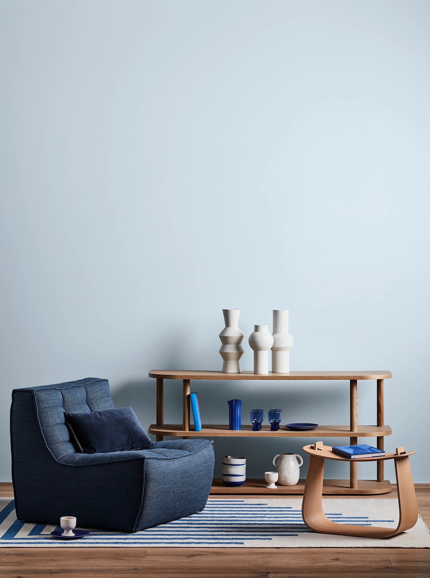 Blue living room with blue armchair, wooden coffee table and shelves with blue and white decor. 