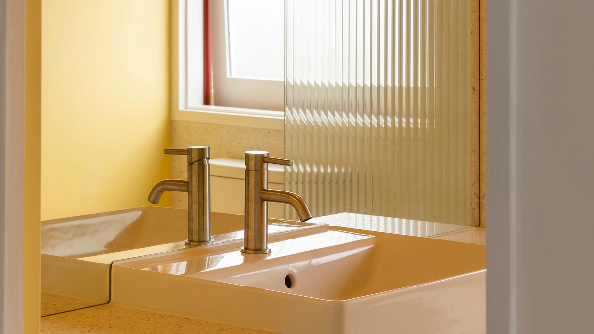 Bathroom sink with mirror behind in bathroom in yellow tones.