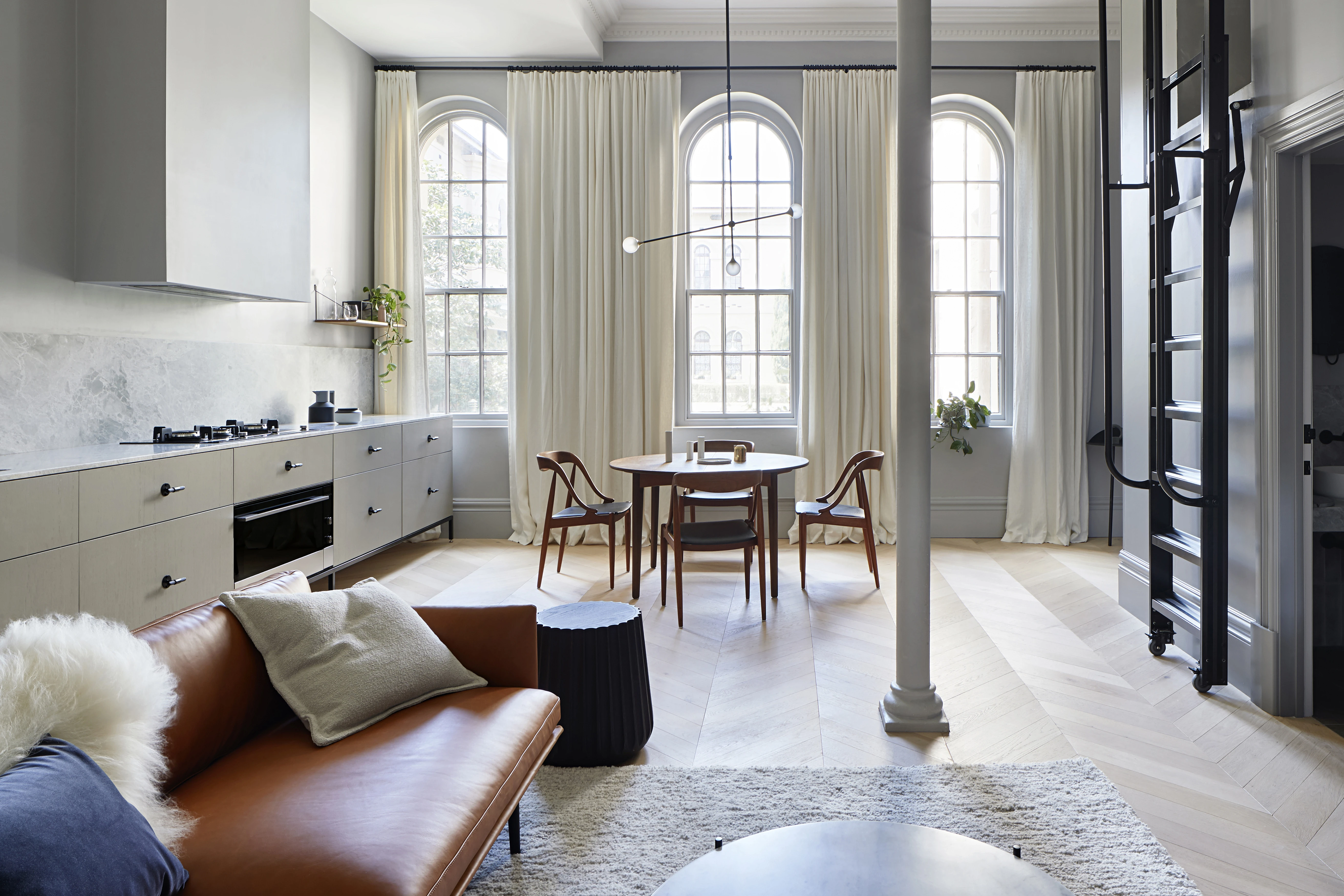 White open plan kitchen, living and dining. Three large arched pane windows with ceiling to floor white curtains