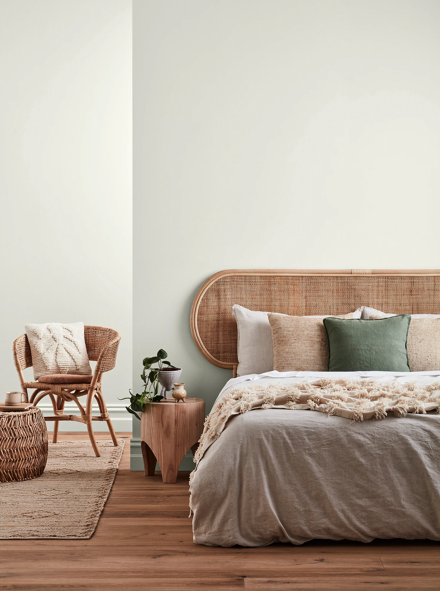 Neutral-coloured bedroom with rattan headboard and chair and neutral linens.