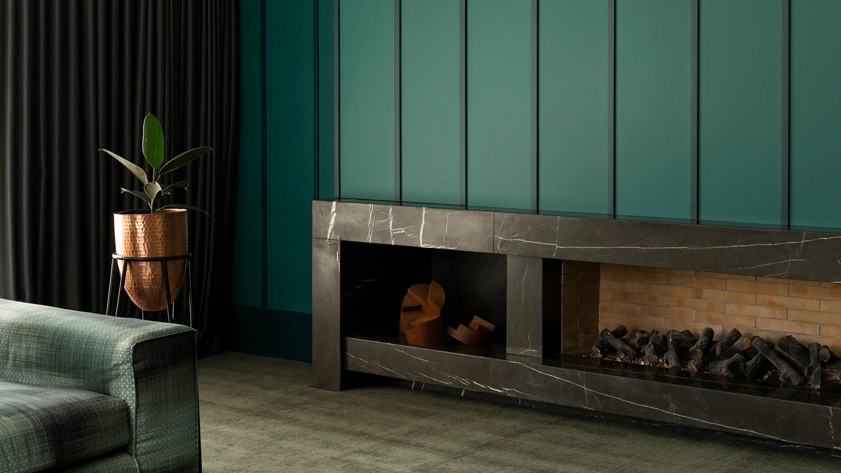 Fireplace inbuilt into wall with green paneling above. Potted plant to left.