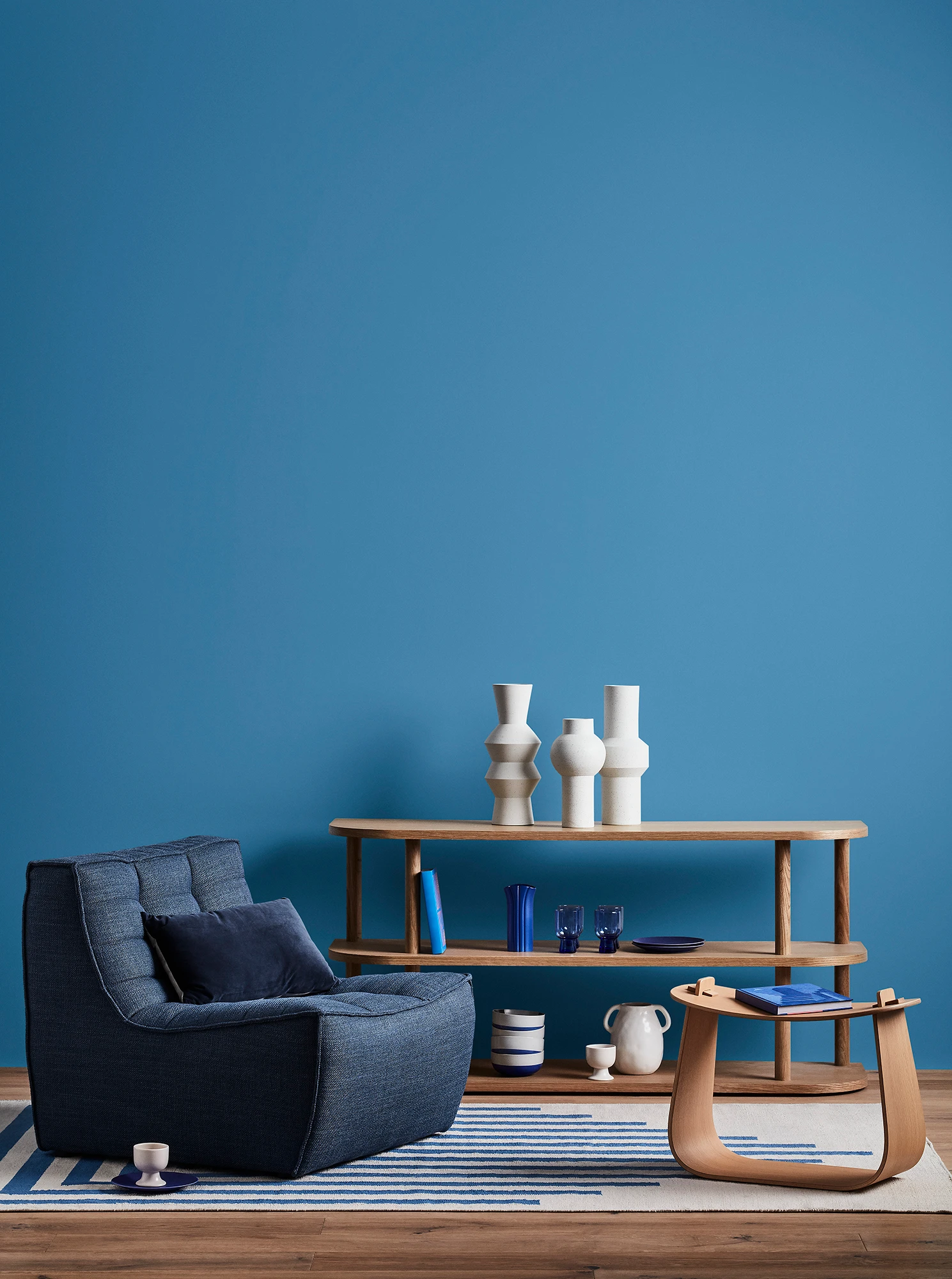 Blue living room with blue armchair, wooden coffee table and shelves with blue and white decor.