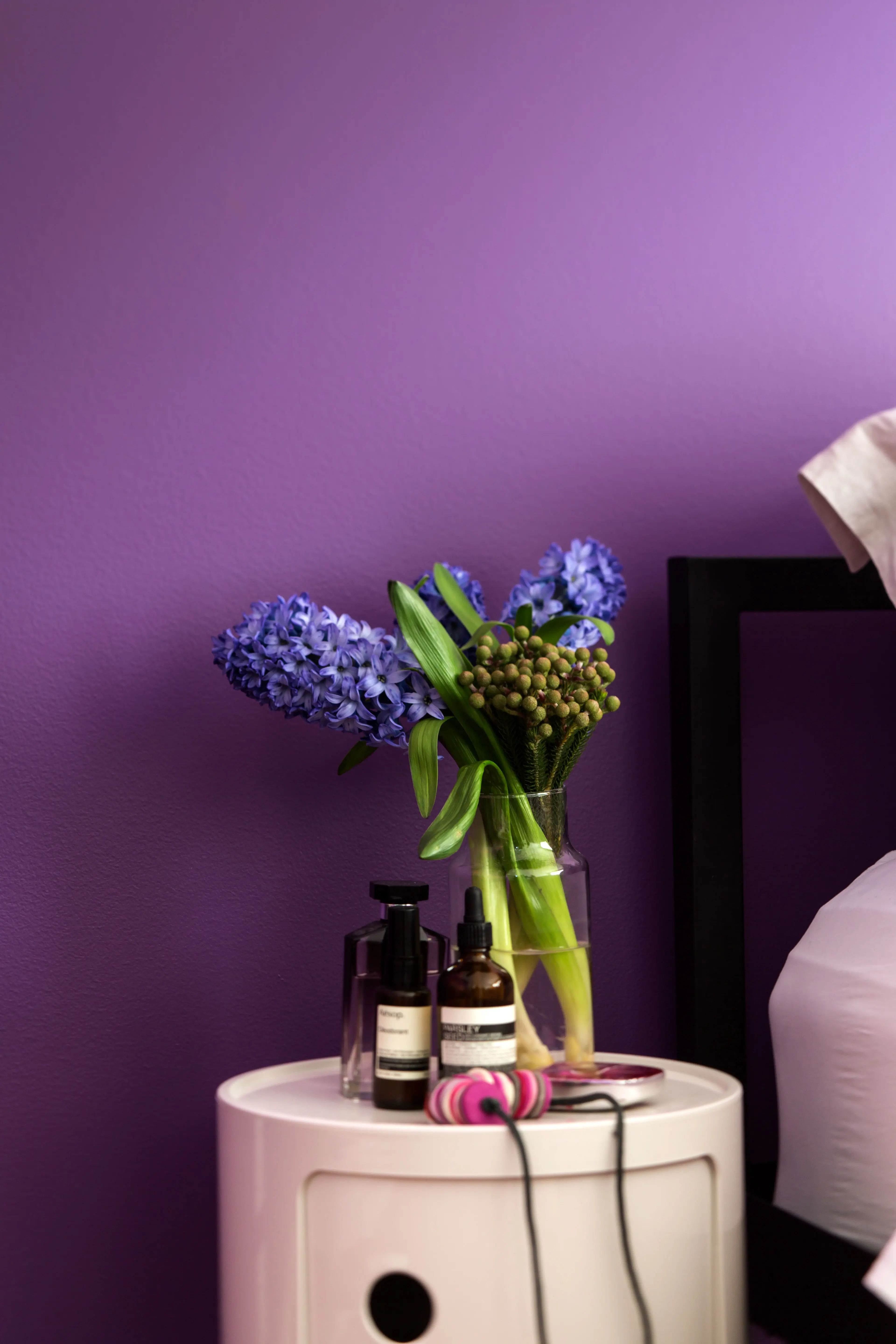 Hyacinth flowers on white bedside table in purple bedroom.