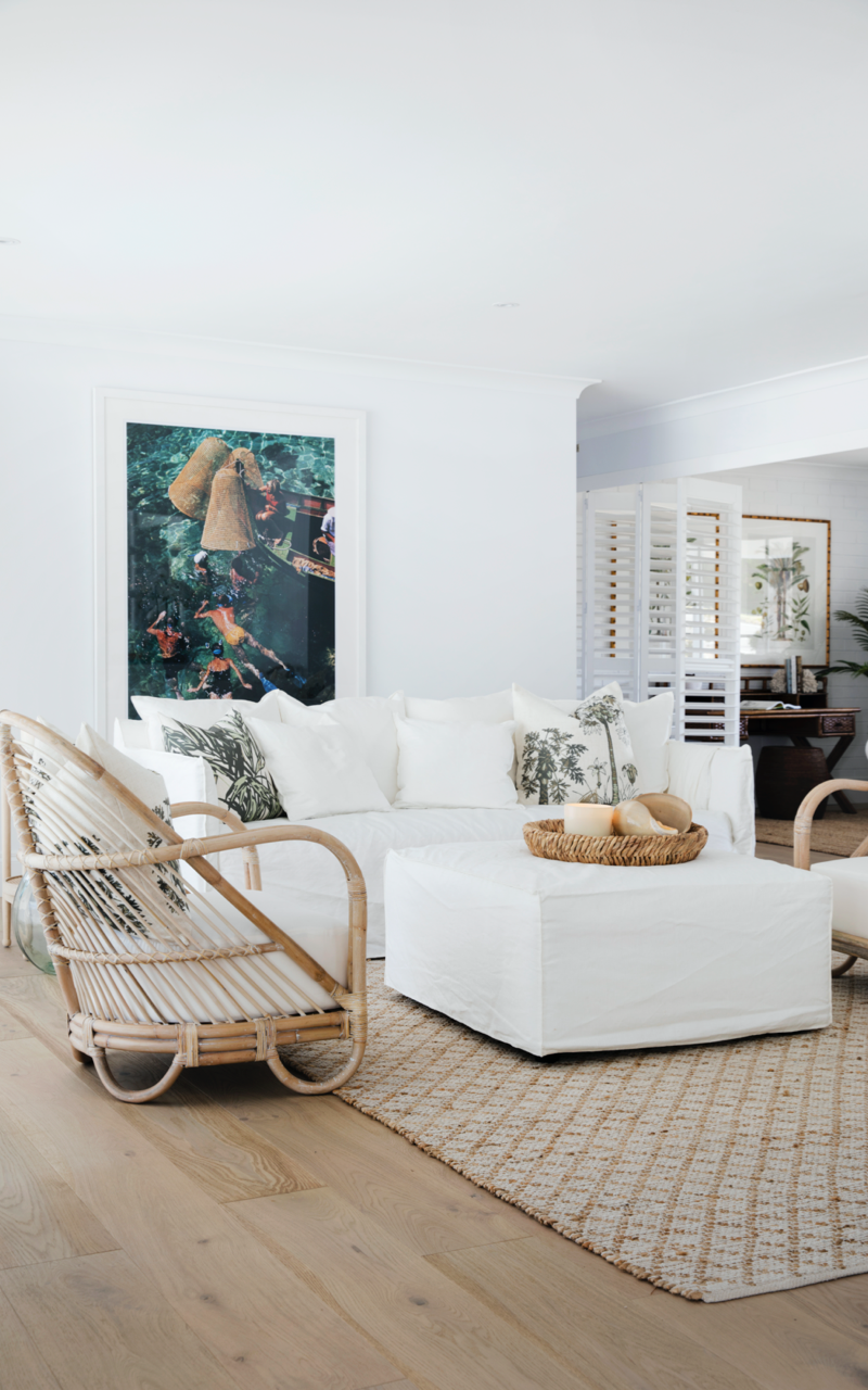 Living room in Dulux White on White™. Colour Me Hamptons by Three Birds Renovations. Colourful artwork, cane furniture and white couch.