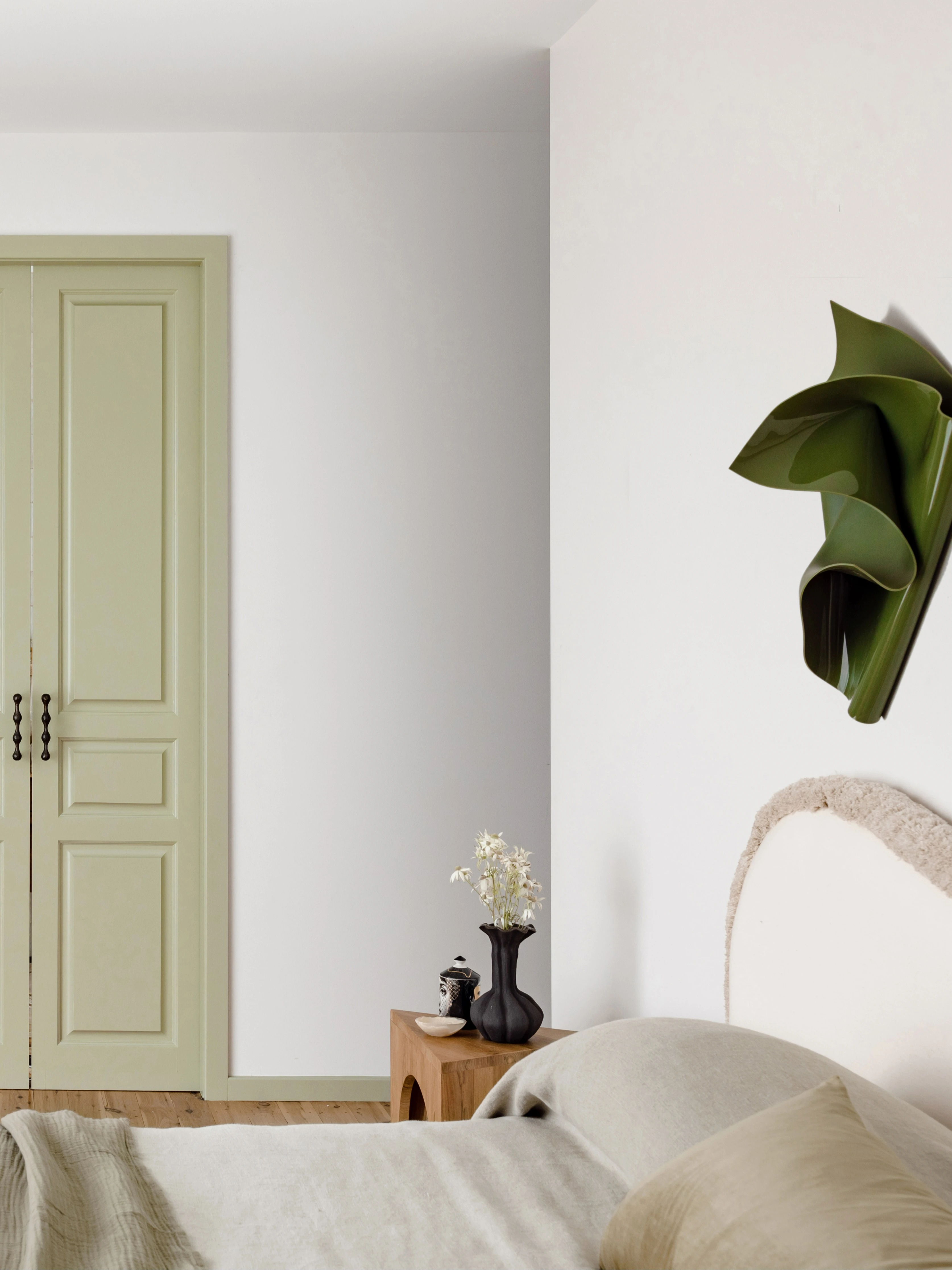 White bedroom with green door and green wall art