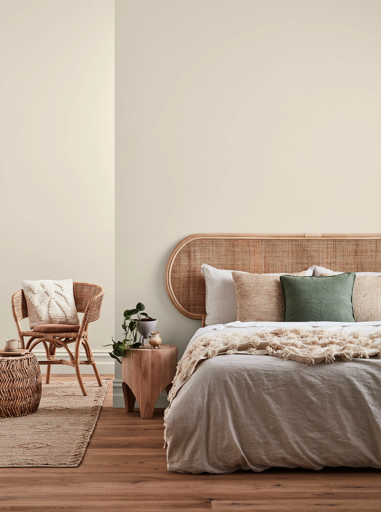 Neutral-coloured bedroom with rattan headboard and chair and neutral linens.