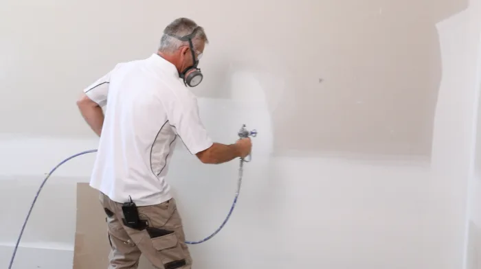 Trade painter spray painting white interior wall with spray gun