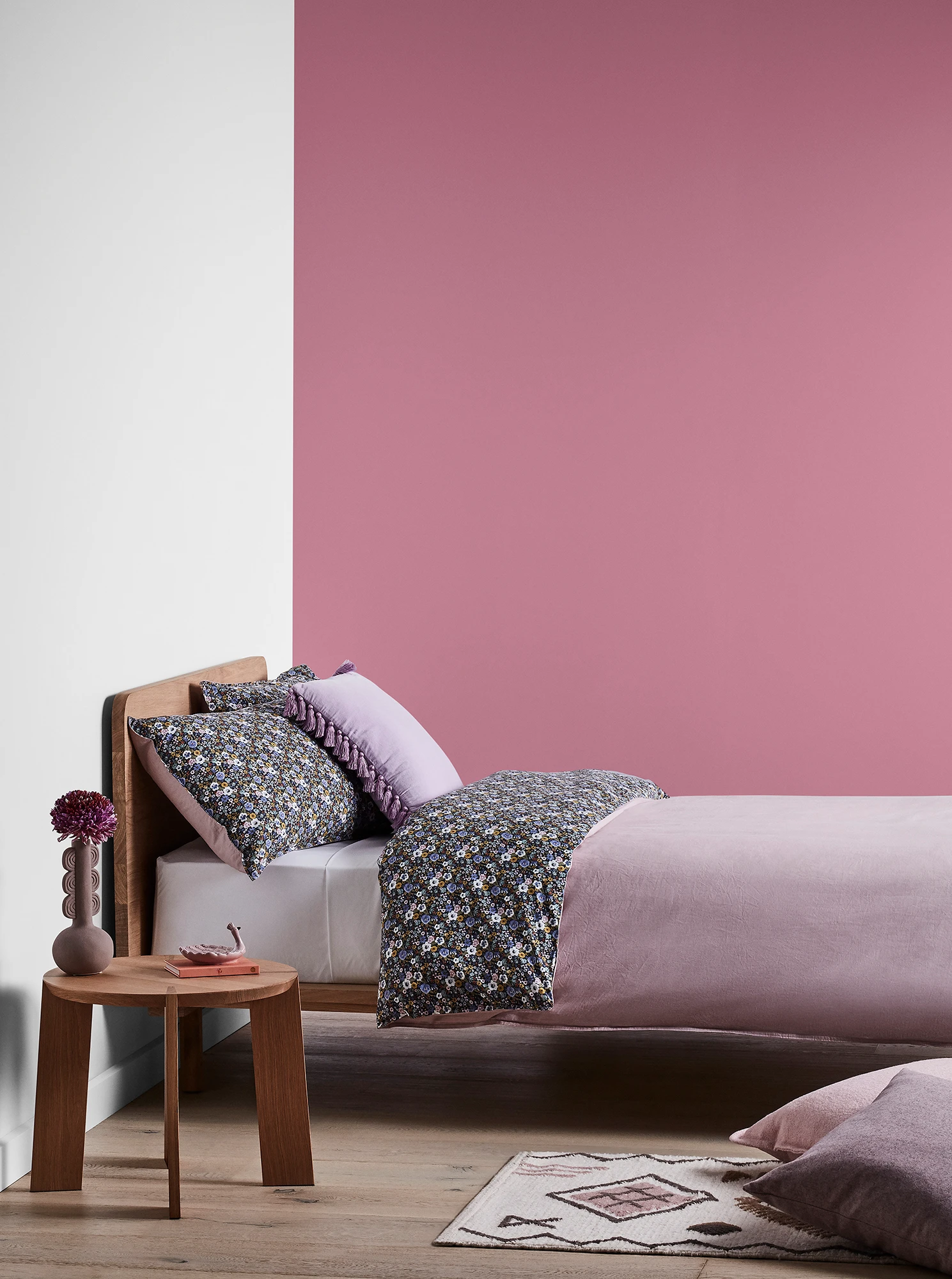 Purple-pink bedroom with timber bed and side table and purple linens.