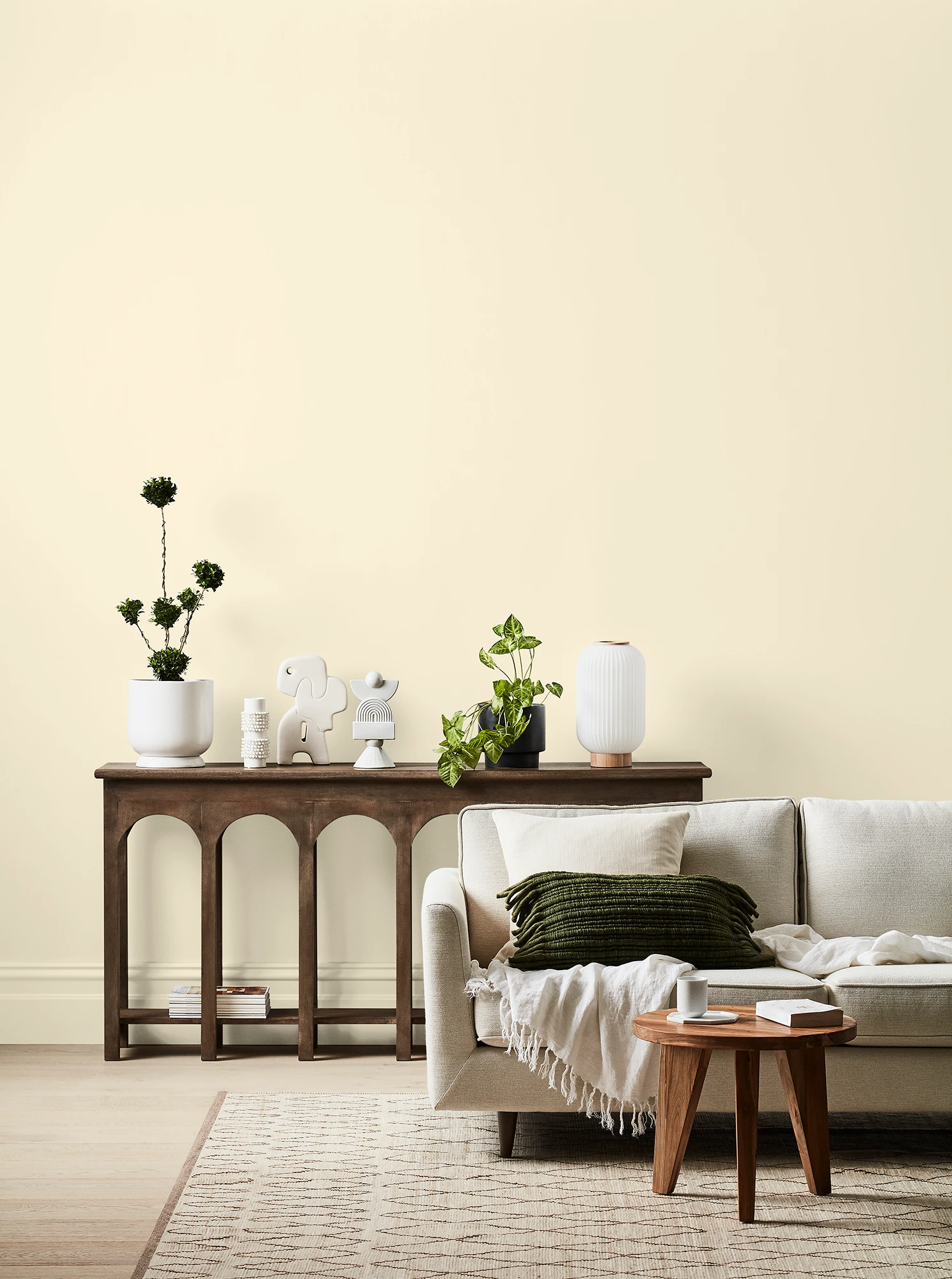 White living room with cream couch, timber side table and timber table with ornaments and plants.