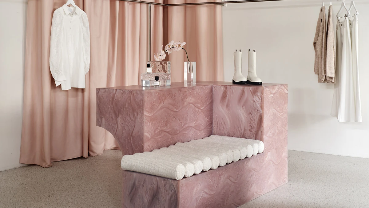 Pink marble stone bench in middle of room with curtains against wall in background.