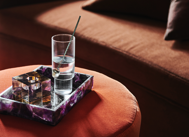 Closeup of glass, candleholder and purple tray decor on a velvet footstool 