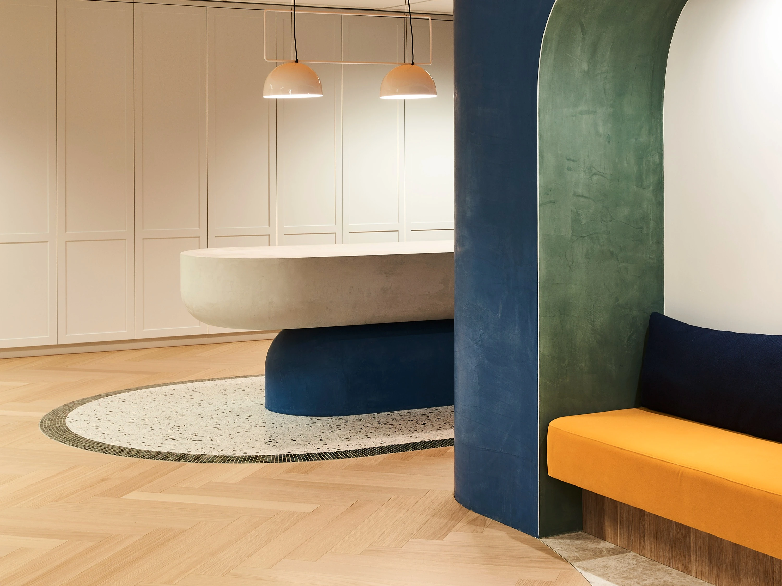Modern office waiting area with curved stone coloured table and orange bench seat