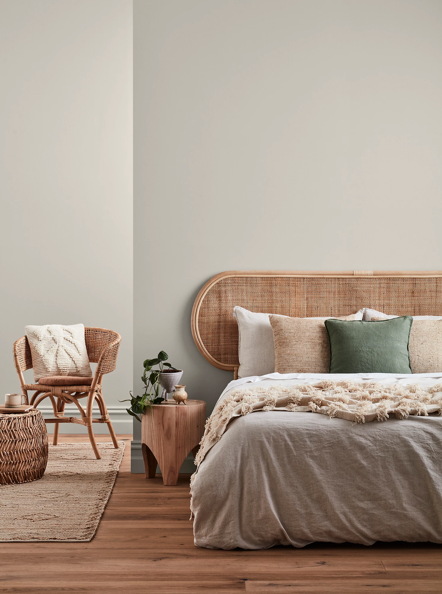 Neutral-coloured bedroom with rattan headboard and chair and neutral linens.