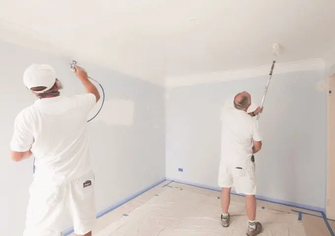 Two painters spray painting and back rolling a ceiling