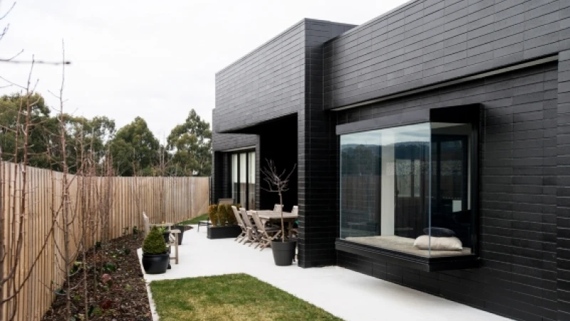 Side of black brick house with glass box windows