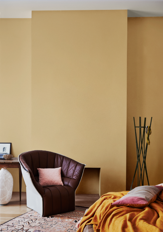 Dulux Buttercookie painted room with purple velvet armchair, black modern hat stand and empty fireplace. 