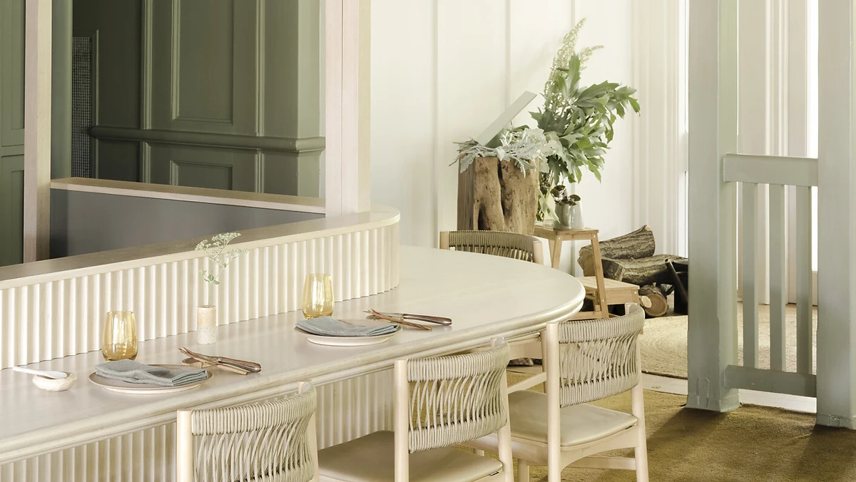 Curved benches with plates set, plants and chair in background room. Light, cream styled design. 
