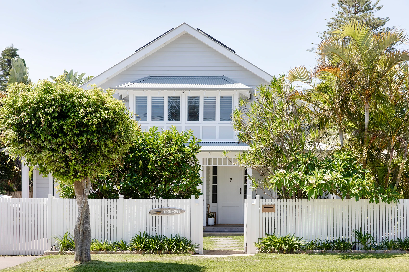 Exterior of grey and white weatherboard house with picket fence.