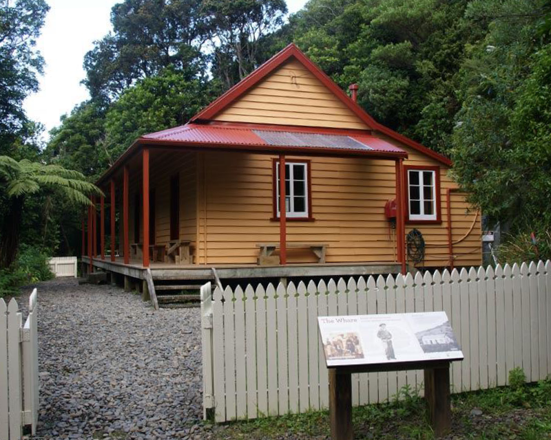 A whare with orange weatherboards and a red roof