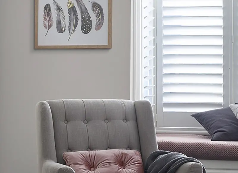 A chair in a lounge with a pink cushion. There's a framed photo of feathers on the wall. 