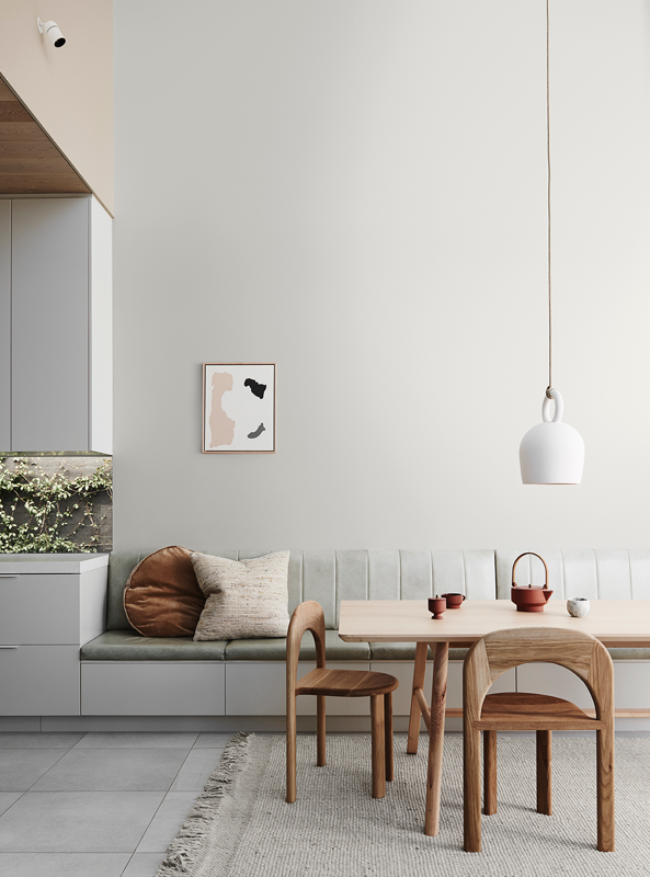 Rust-coloured teapot, tea cup and sugar bowl on a neutral-colour dining table with a bench seat and wooden chairs in dining room with white walls and white pendant light. 