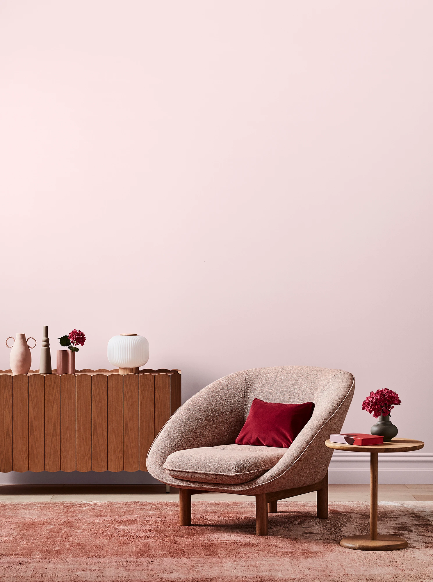 Light pink living room with pink armchair, wooden side table and sideboard with white and pink decor.