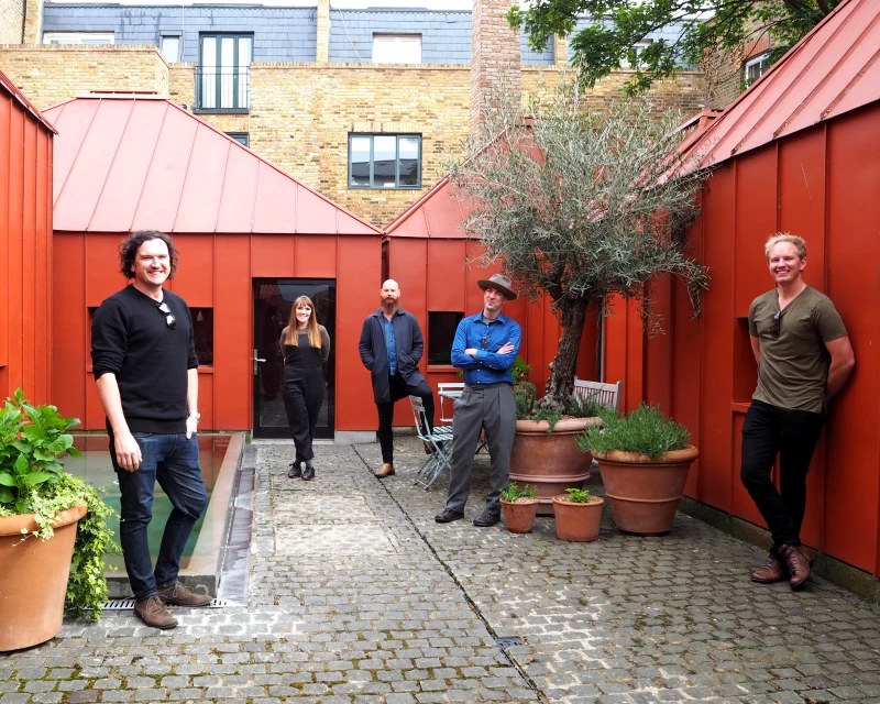 People in courtyard surrounded by single storey red buildings