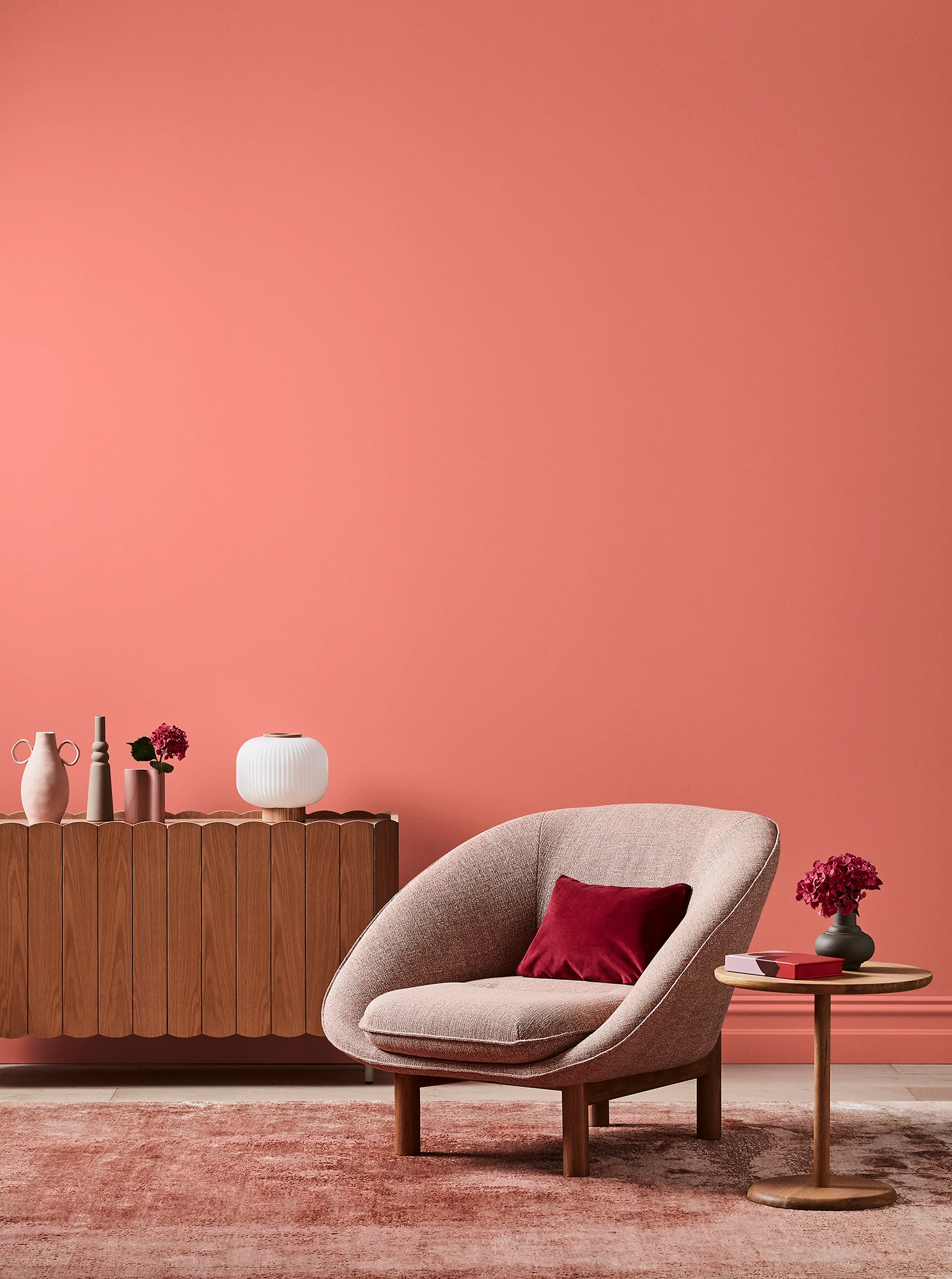 Orange-pink living room with pink armchair, wooden side table and sideboard with white and pink decor.