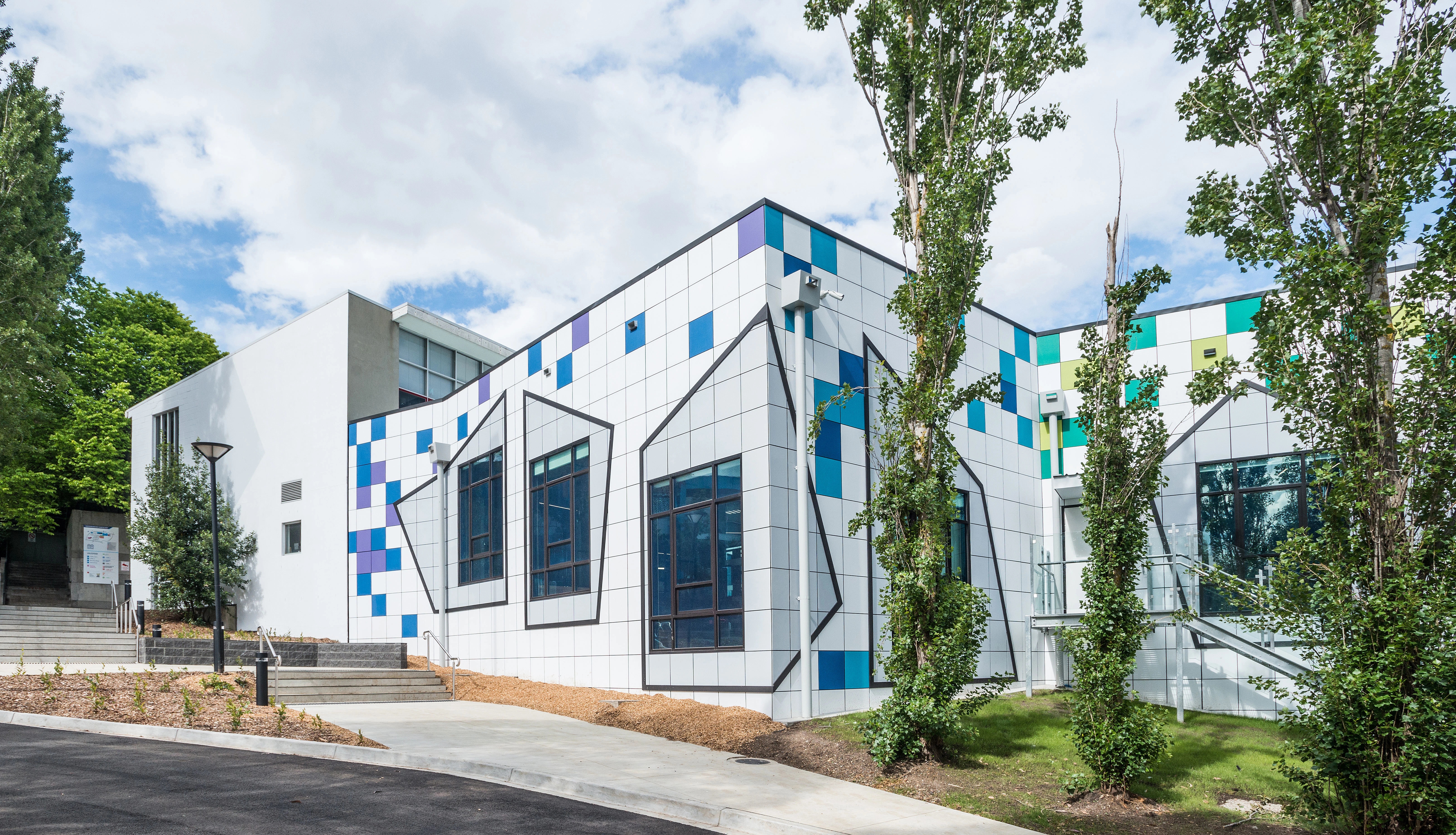 exterior of high school building. White with random scattering of blue, purple, green and lime tiles