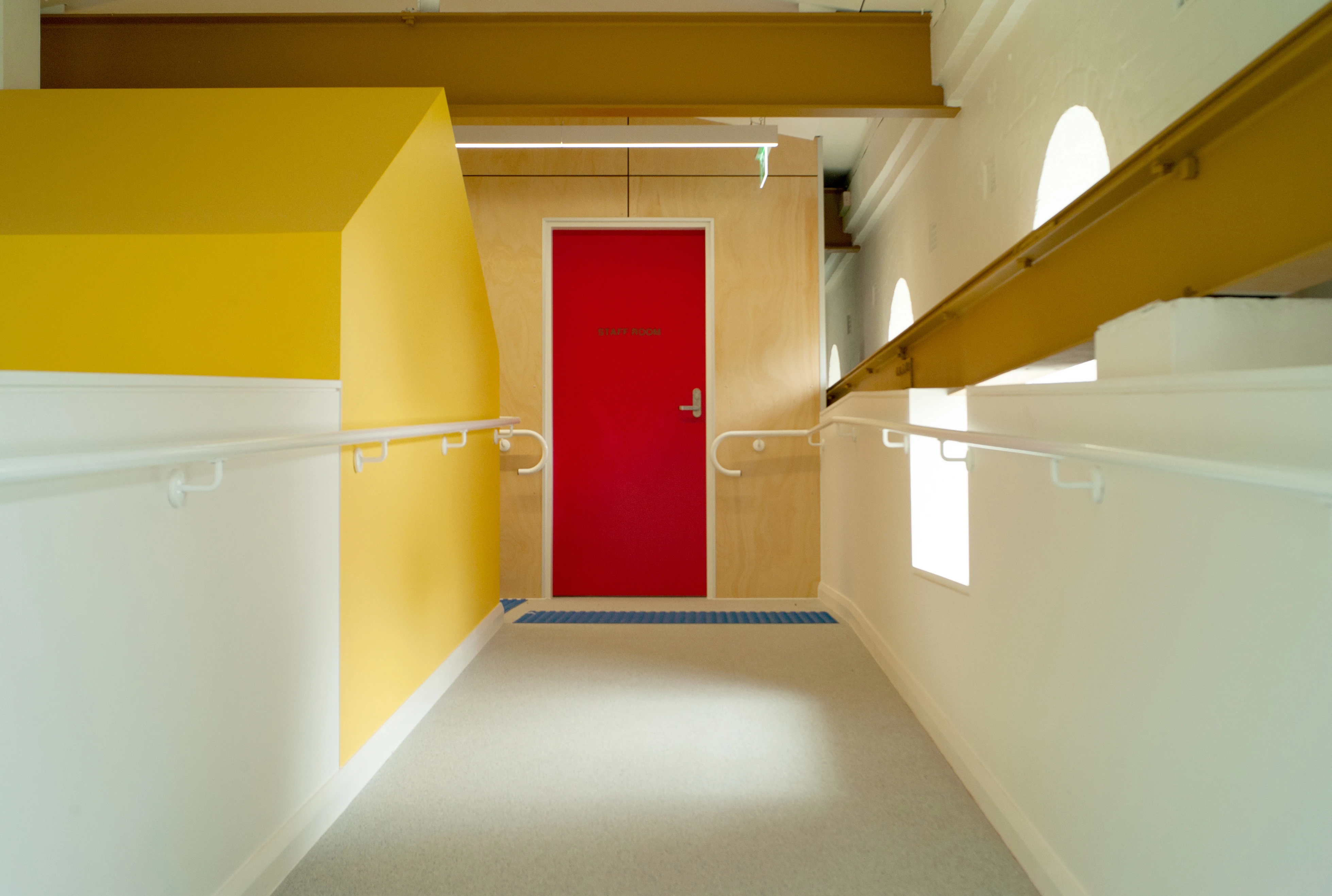 Yellow and white ramp hallway with red door at end.