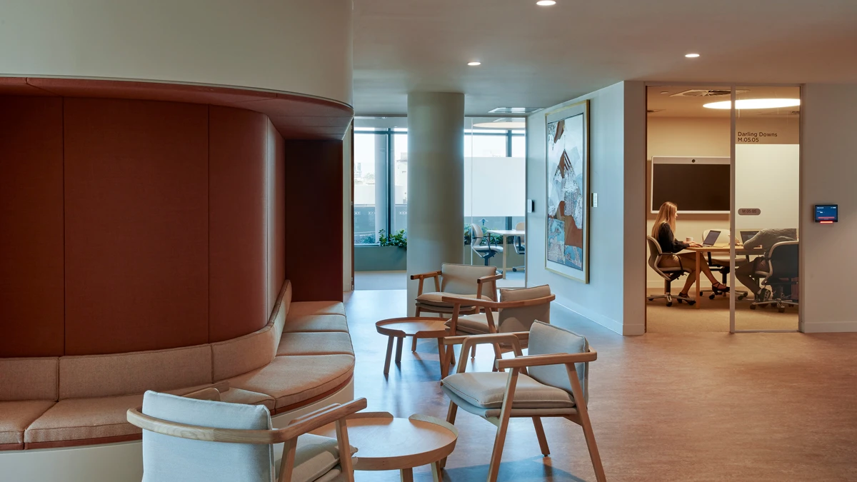 Seating area with cushioned seating along wall and chairs with small tables. Meeting room in back.