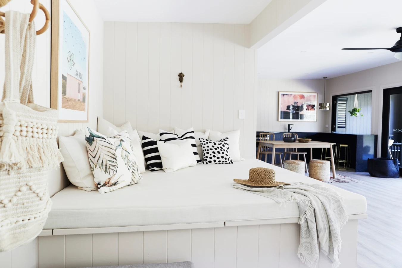 Neutral coloured living area with walls in Dulux Parchment Paper and ceiling in Dulux Summer Cloud Quarter. Kitchen with black benches and cabinets, timber dining setting.