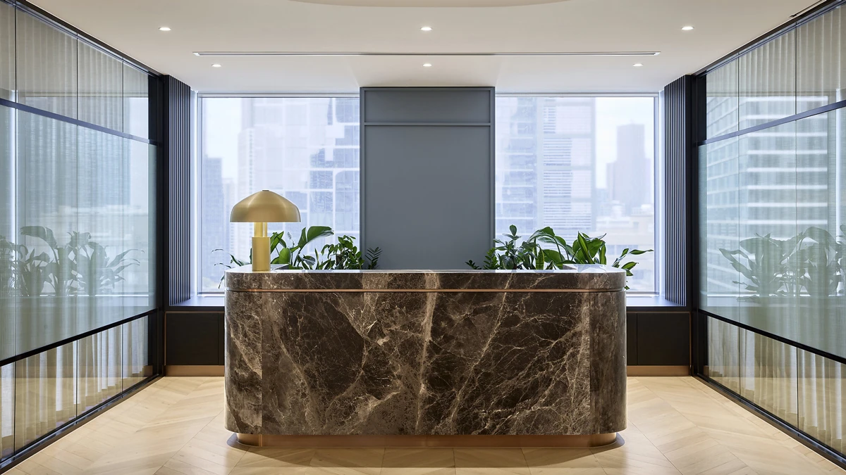 Marble reception desk with lamp on top. Plants and window in background. 