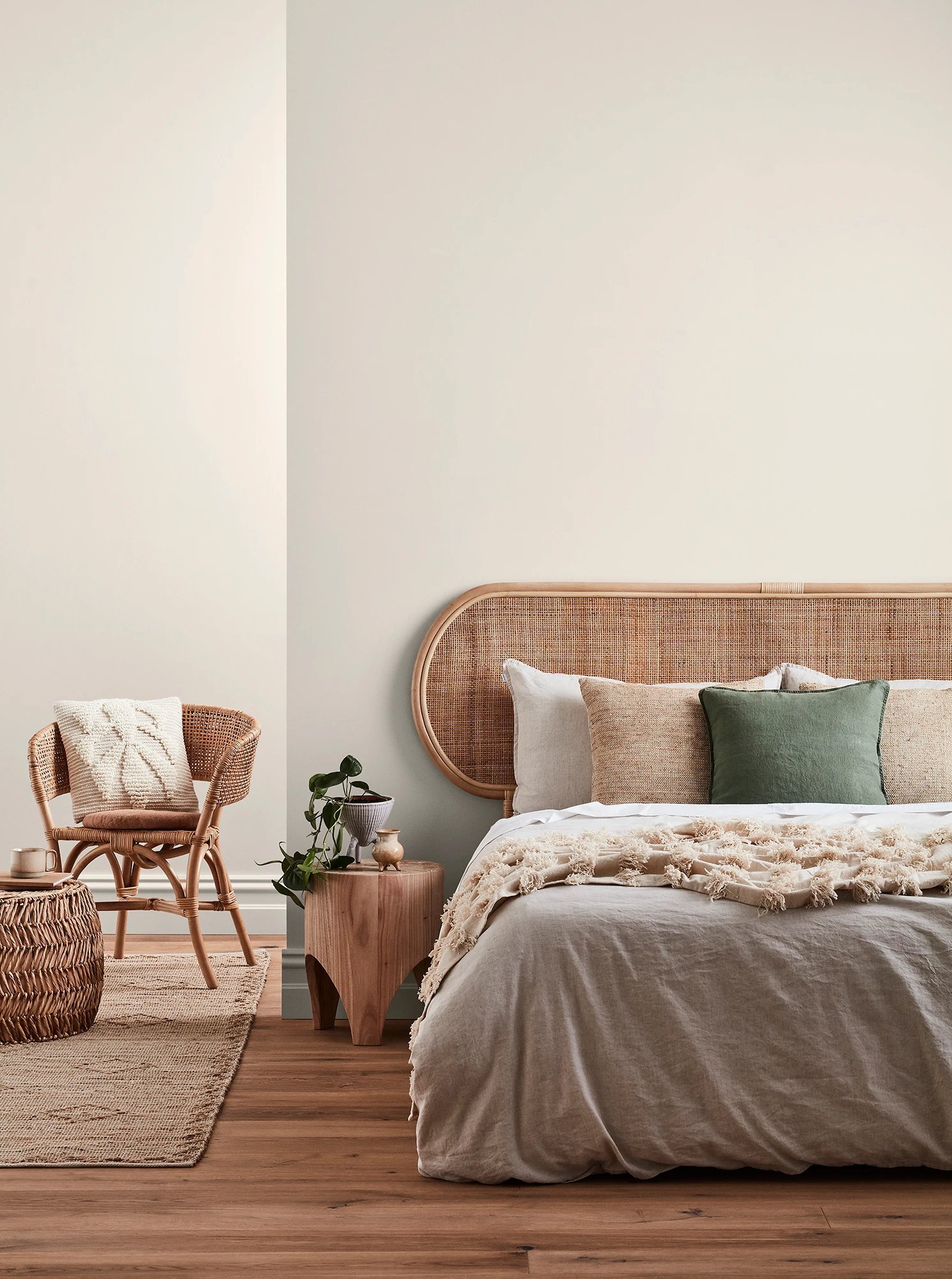 Neutral-coloured bedroom with rattan headboard and chair and neutral linens.