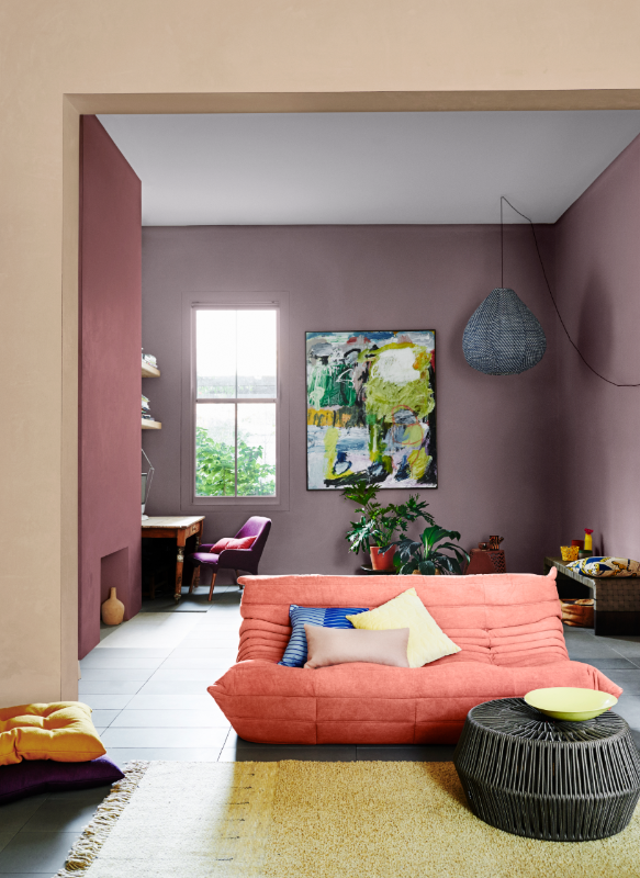 Lounge room with pink couch and blue, pale pink and yellow cushions, yellow rug, purple chair and brown cane coffee table. Walls in Dulux Manila, Forest Fruit Pink and Punctuate.