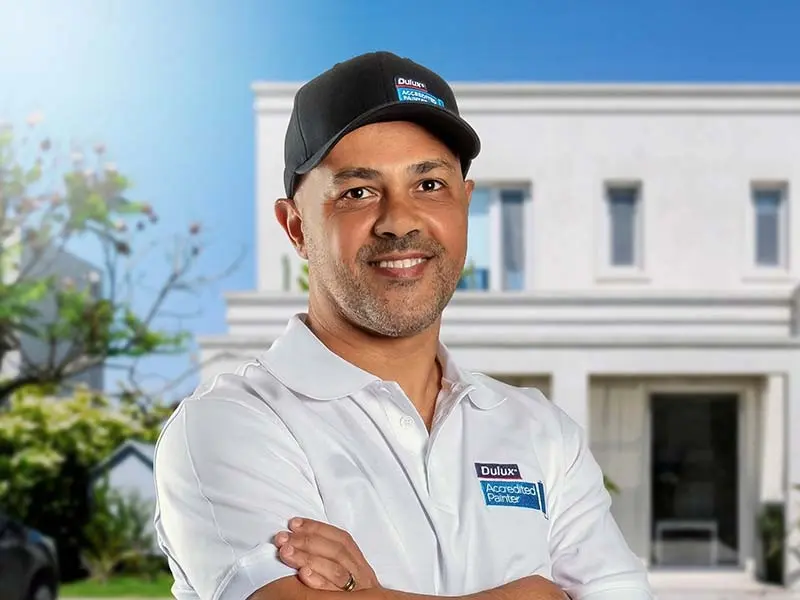 A man with his arms crossed wearing a Dulux Accredited painter cap and white Dulux Accredited painter shirt