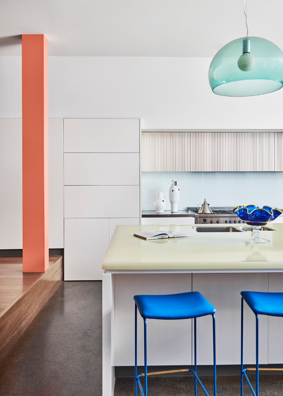 White kitchen with orange column, island bench with bright blue stools