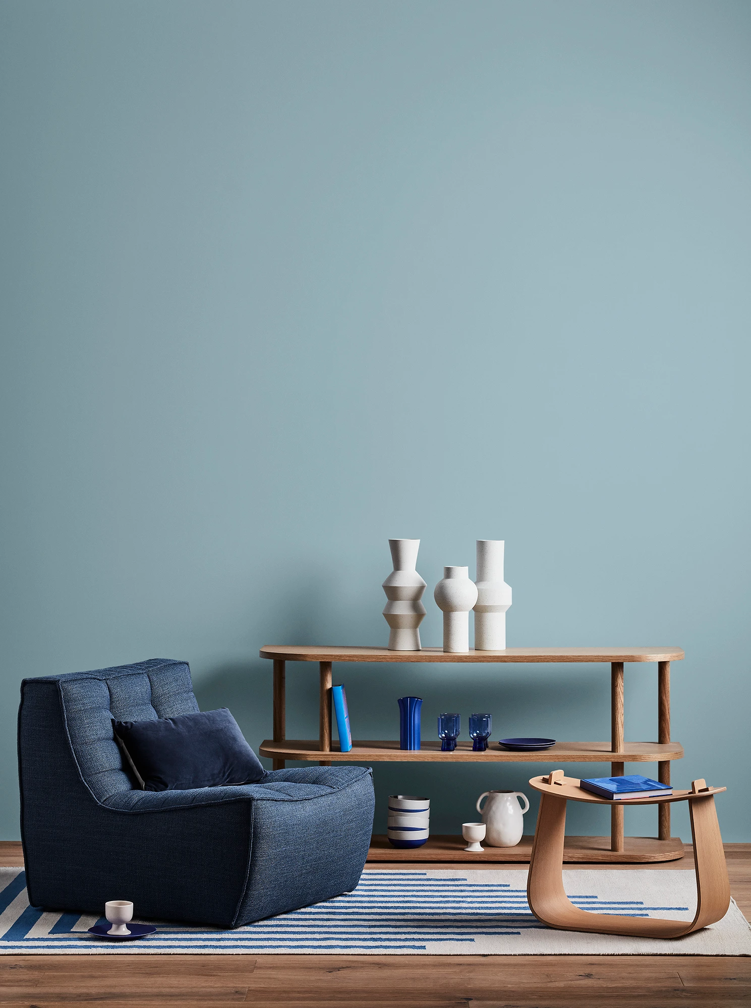 Blue living room with blue armchair, wooden coffee table and shelves with blue and white decor. 